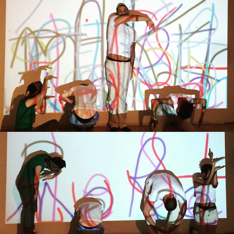 Actors fold their bodies to create letters against a projected background of scribbled letters